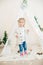 Little cute girl in a white warm knitted cardigan near a children`s lodge decorated with a garland and needles, toys