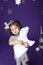 Little cute girl in white winter wreath and with toy polar bear having fun in studio on purple background with silver Christmas