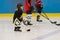 The little cute hockey girl is on the ice wearing in full equipment: hockey helmet, gloves, stick, skates. Figures of two teenager