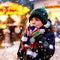 Little cute kid boy drinking hot children punch or chocolate on German Christmas market. Happy child on traditional