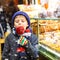 Little cute kid boy near sweet stand with gingerbread and nuts. Happy child eating on apple covered with red sugar