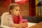 A little cute kid sits in a highchair, holds a glass of juice with his hands and drinks from a straw. in the background