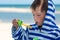 A little cute kid in a striped robe blows soap bubbles against the background of the sea and washed spit,