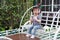 Little cute lovely girl Chinese child smile and play sit on a white benches hold a lollipop and flower at summer park nature