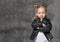 Little cute smiling blond girl in stylish rock style black leather jacket, jeans and white sneakers standing in confident pose