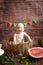 Little cute toddler with blond hair sits in basket with watermelon on a dark wooden background. Children and fruits.