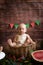 Little cute toddler with blond hair sits in basket with watermelon on a dark wooden background. Children and fruits.