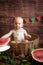 Little cute toddler with blond hair sits in basket with watermelon on a dark wooden background. Children and fruits.