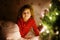 Little cute toddler girl in bed under Christmas tree and dreaming of Santa at home, indoors. Traditional Christian