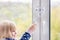 Little cute toddler girl trying to open window in apartment at high-tower building. Children window protection lock. Cable safety