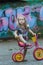 Little cyclist girl wearing checked tunic riding yellow and pink tricycle