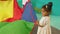 Little dark-skinned girl in dress holding one corner of rainbow play parachute during playtime in nusery. Multiracial
