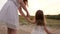 A little daughter in a white dress is walking with her mom`s hand along the road. Evening walk of a woman and a child