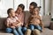 Little daughters sit on parents laps talking resting on couch