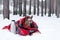 Little dog with big ears wrapped in red checkered plaid on a snow. Picnic in winter forest with hot tea in thermos and cup