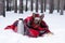 Little dog with big ears wrapped in red checkered plaid on a snow. Picnic in winter forest with hot tea in thermos and cup