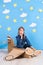 Little dreamer girl playing with a cardboard airplane at the studio with blue sky and white clouds background.