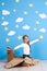 Little dreamer girl playing with a cardboard airplane at the studio with blue sky and white clouds background.