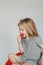 A little European girl is sitting on a red chair and eating a juicy large strawberry. gray background