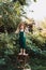 Little farmer in green overalls, standing in garden with happy face, in straw hat