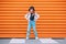 Little fashion-dressed girl portrait sincerely smiling while looking at camera on a pedestrian zebra crosswalk on orange wall