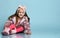 Little female in pink faux fur coat, pants and boots. She smiling, sitting on floor against blue studio background. Close up