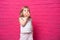 Little funny blonde girl in white shirt eats donut on pink background