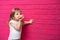 Little funny blonde girl in white shirt eats donut on pink background