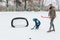 Little funny boy with her mother skating in the park. Play ice hockey with stick and goal. Outdoor. Winter sport
