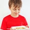 Little funny boy in a red shirt eating instant noodles using fork on white background