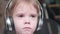 A little funny boy sits in a chair and listens to music through headphones. Face close up