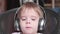 A little funny boy sits in a chair and listens to music through headphones. Face close up