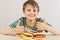 Little funny boy in a striped shirt at the table recommends hamburgers and sandwich on white background