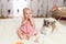 Little funny Caucasian girl the child sits at home on the floor on a light carpet with the best friend of the half-breed dog with