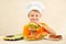 Little funny chef in chefs hat enjoys cooking tasty hamburger