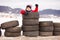 Little funny child in red jacket standing inside used tires among the road mountain view on background