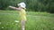 Little funny cute blonde girl child toddler in yellow bodysuit and white hat walking in field with green grass and