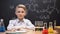 Little genius sitting in protective glasses, chemical liquids in tubes on table