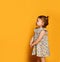 Little ginger toddler girl with two ponytails, in gray polka dot dress. Smiling while posing sideways on orange background