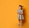 Little ginger toddler girl with two ponytails, in gray polka dot dress, white sandals. Child smiling, posing on orange background