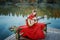 Little Gipsy girl in the red dress on the shore of the lake with a guitar