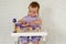 Little girl 1 years playing with doll house furniture. Cute baby girl in violet dress. Violet style