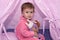Little girl 2 years old plays in wigwam or tent in children`s room with colorful toys