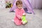 Little girl 2 years old plays in wigwam or tent in children`s room with colorful toys