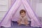 Little girl 2 years old plays in wigwam or tent in children`s room and smiling