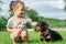Little girl 3-4 sit and pet black-brown dachshund dog in collar, on green grass