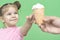 Little girl 4 years old in a pink T-shirt on a green background smiles and reaches out to ice crea