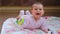 A little girl of 6 months lies on the floor and plays with a rattle.