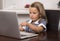 Little girl 6 to 8 years old sitting at home kitchen enjoying with laptop computer concentrated watching internet cartoon movie