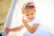 Little girl adjusts her hair of hut for games. Child with beautiful hairstyle in white dress.